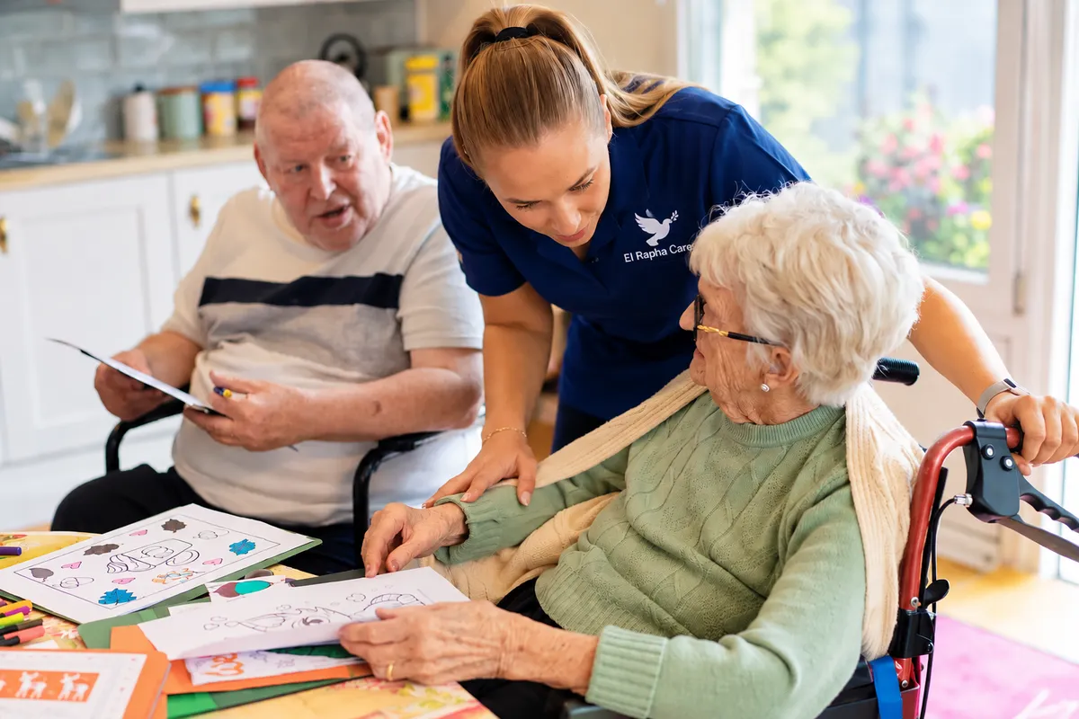Carer helping two older clients with an activity at the table